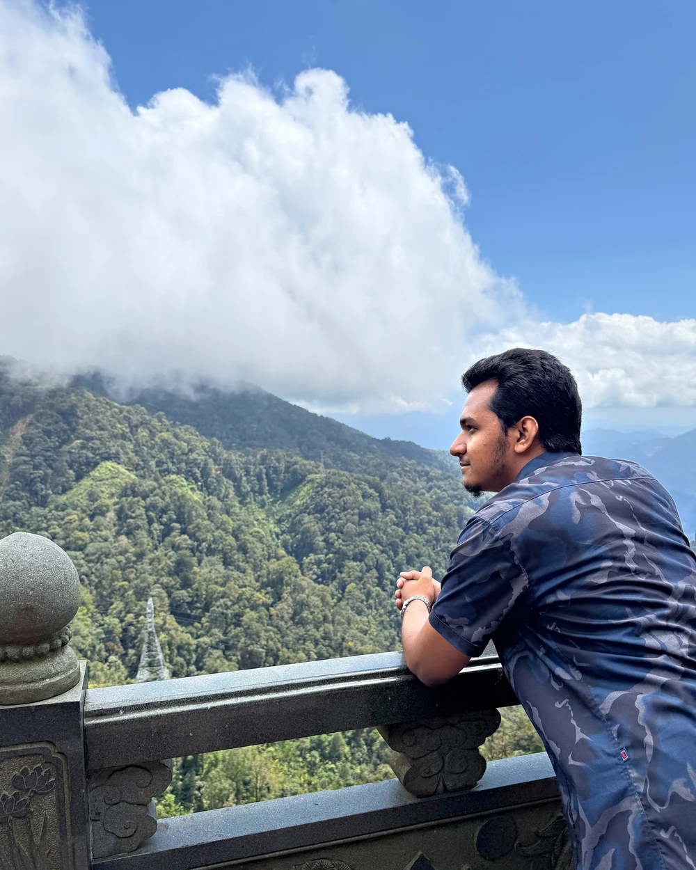 Samir leaning on a stone railing in the mountains, a big cloud rolling over the ridge